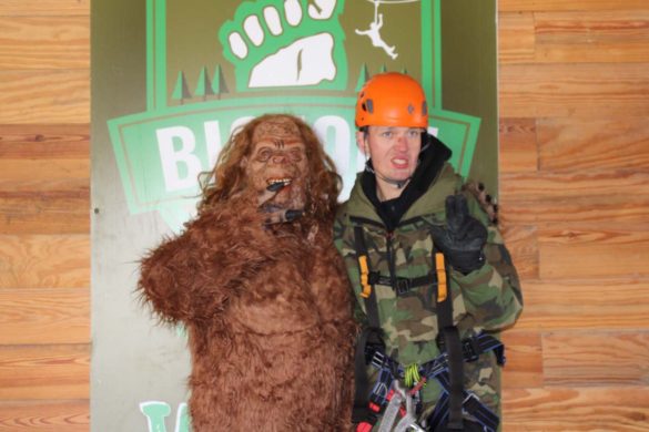 man wearing ziplining equipment posing with bigfoot